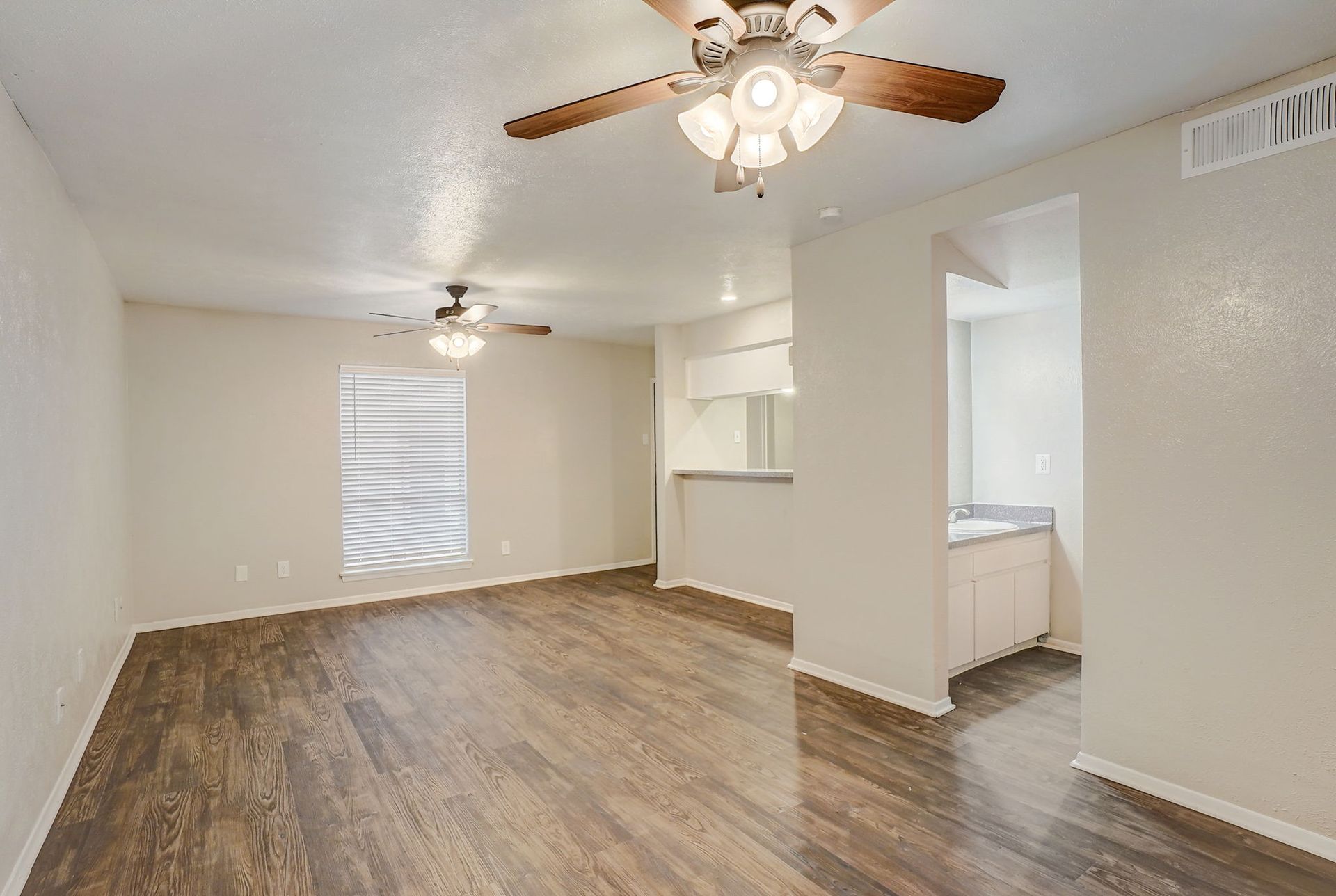 Empty living room with wood-look flooring, ceiling fans, and an open doorway to a bathroom with a vanity.