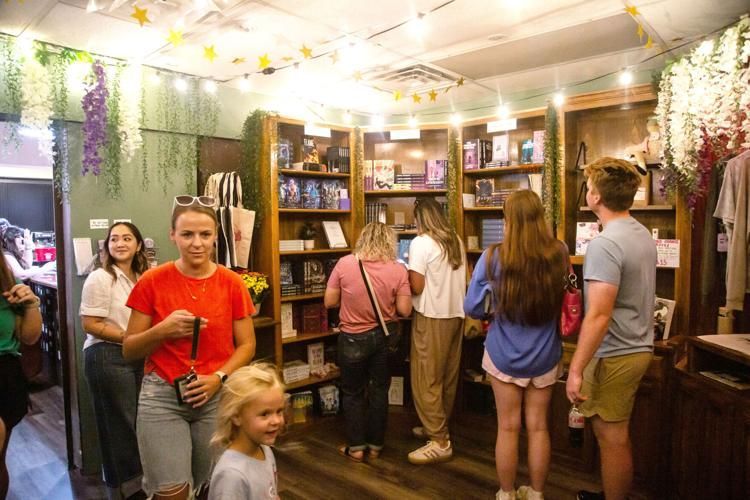 People browse books in a shop. Bookshelves, string lights, and floral decorations are visible.