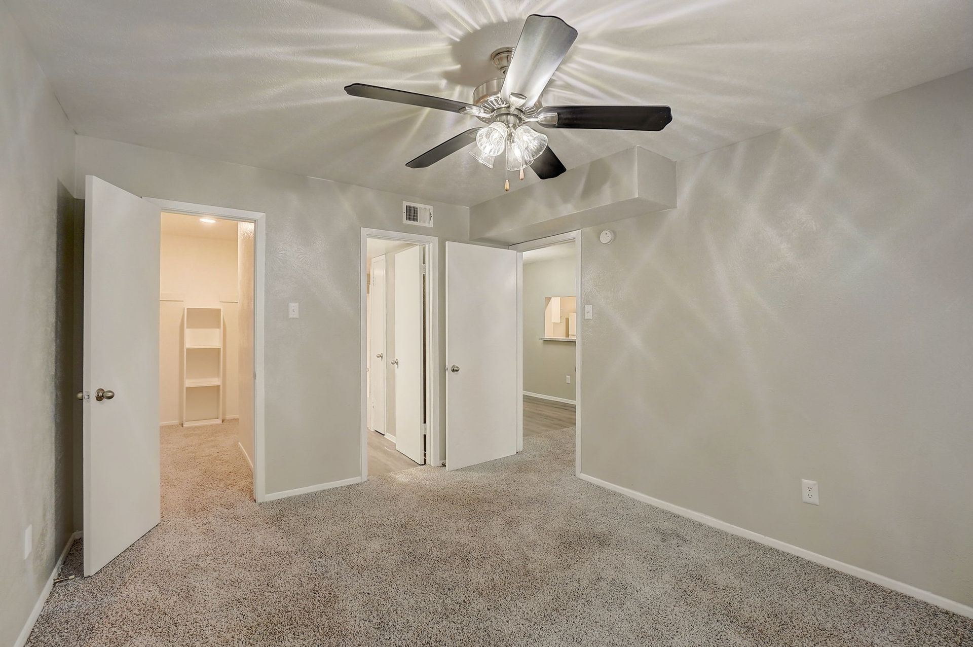 Bedroom with carpet, three doorways, ceiling fan, and white walls.