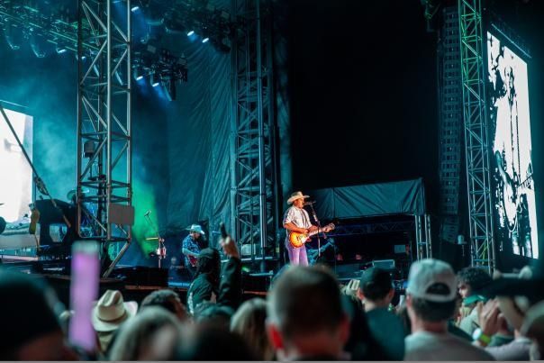 A country musician playing guitar on stage during a concert. Audience in foreground. Green and blue lighting.