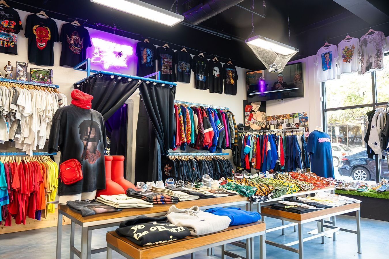 Clothing store interior with t-shirts, jackets, and pants on display. Tables and racks filled with various apparel.