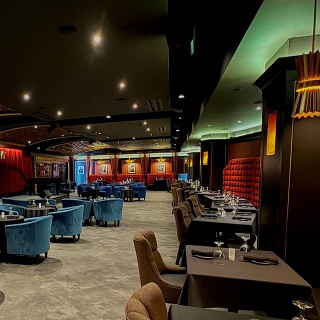 Interior of a dimly lit restaurant with tables set for dining, velvet seating, and dark walls.