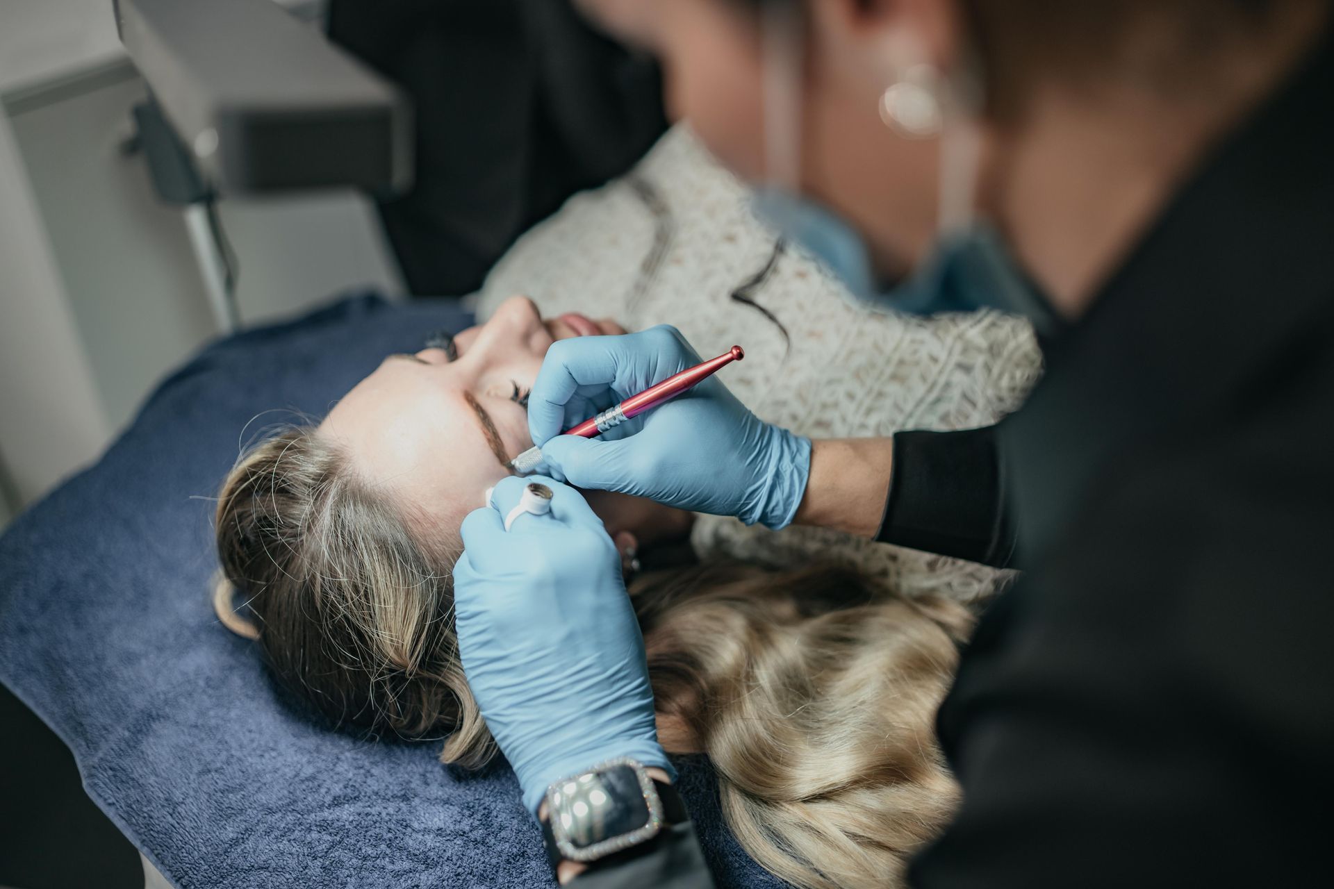 Person, die sich die Augenbrauen microbladen lässt; Kosmetikerin mit blauen Handschuhen