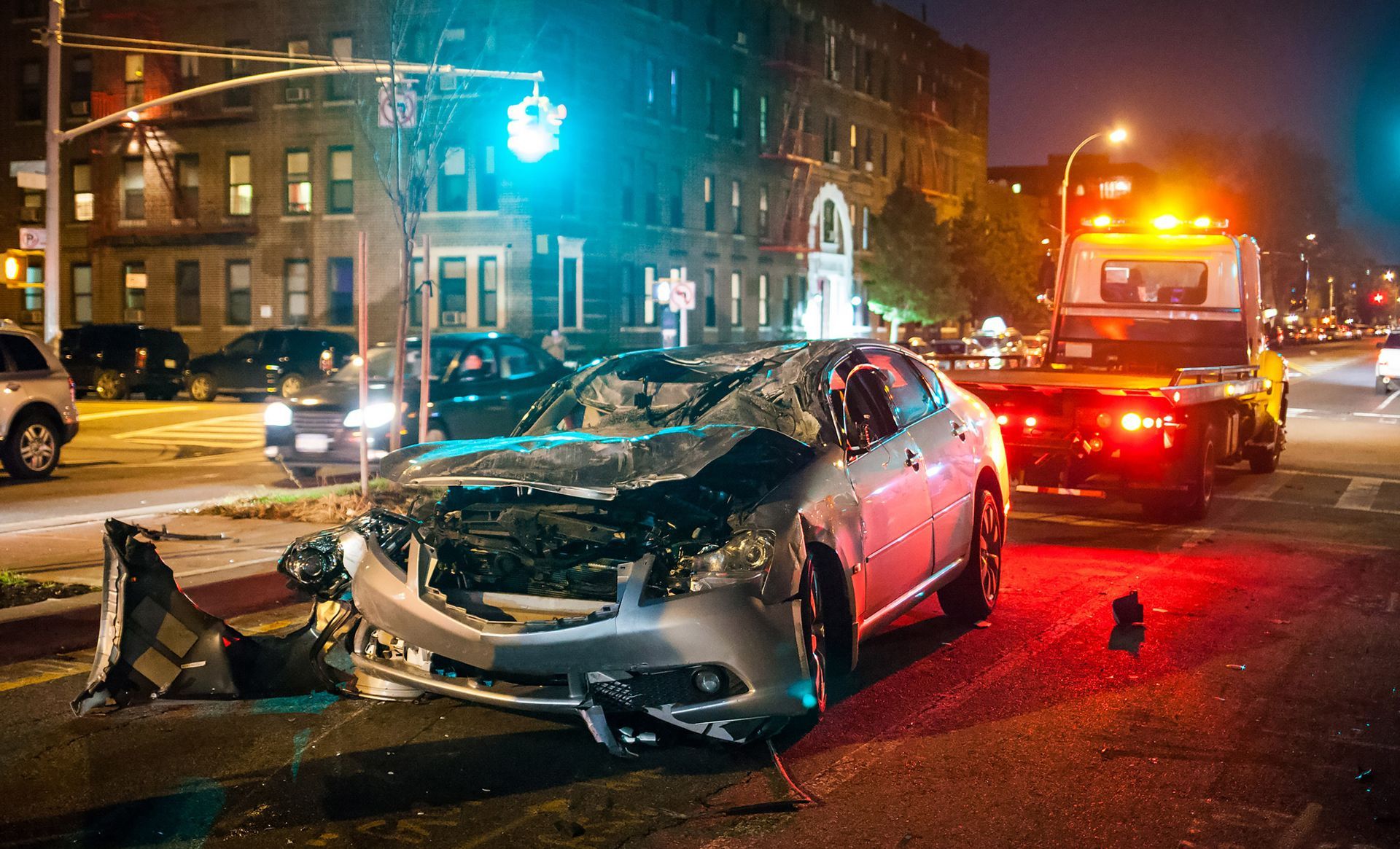 A car accident on a city street at night with a tow truck in the background.