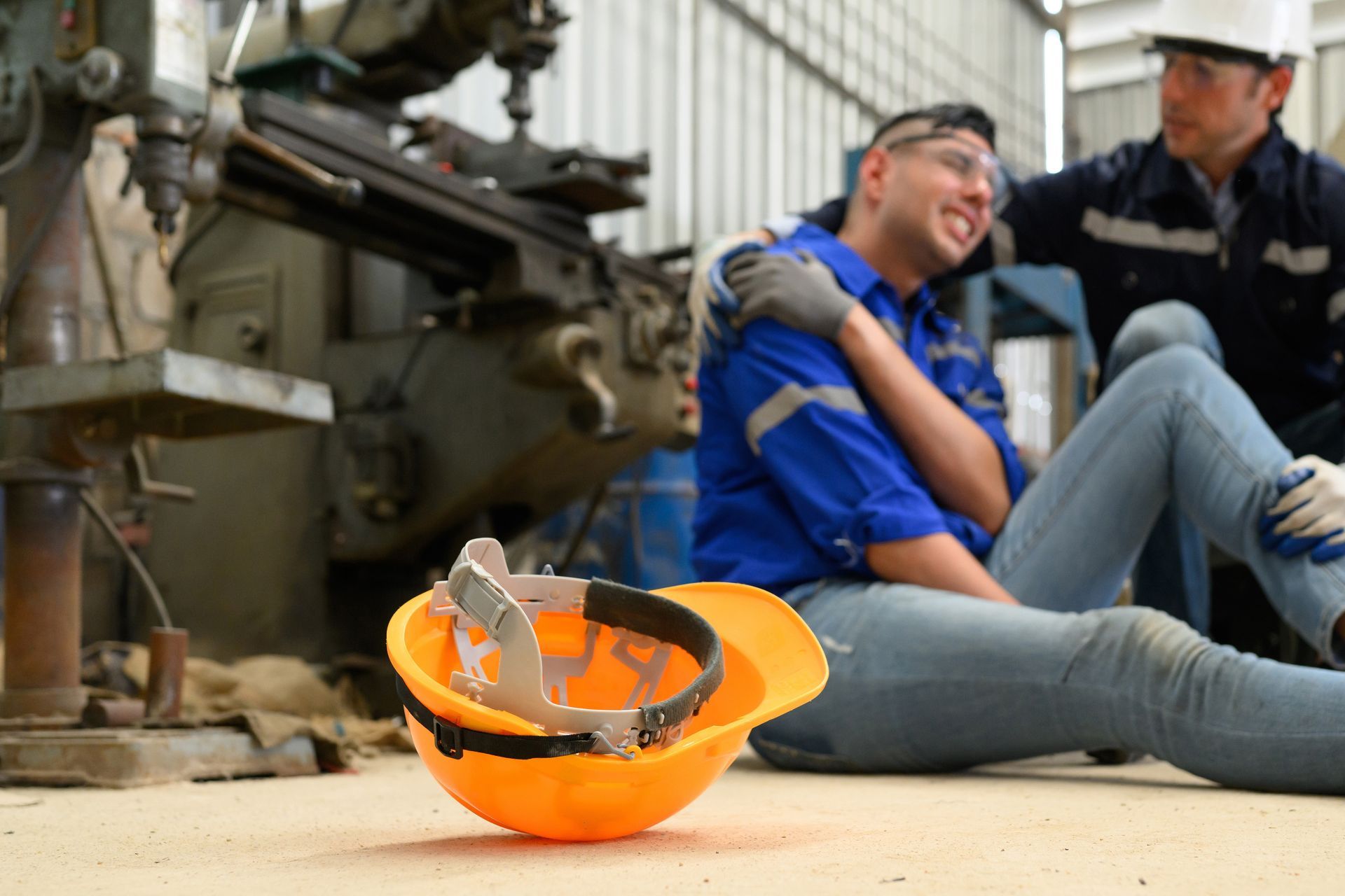 A man is sitting on the floor next to a hard hat.