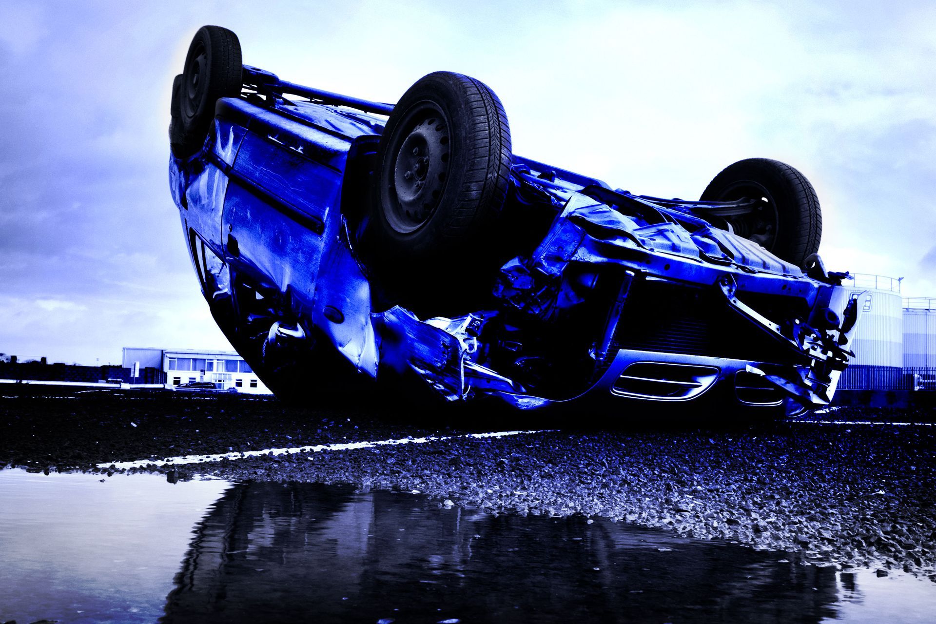 A blue car is upside down in a puddle of water