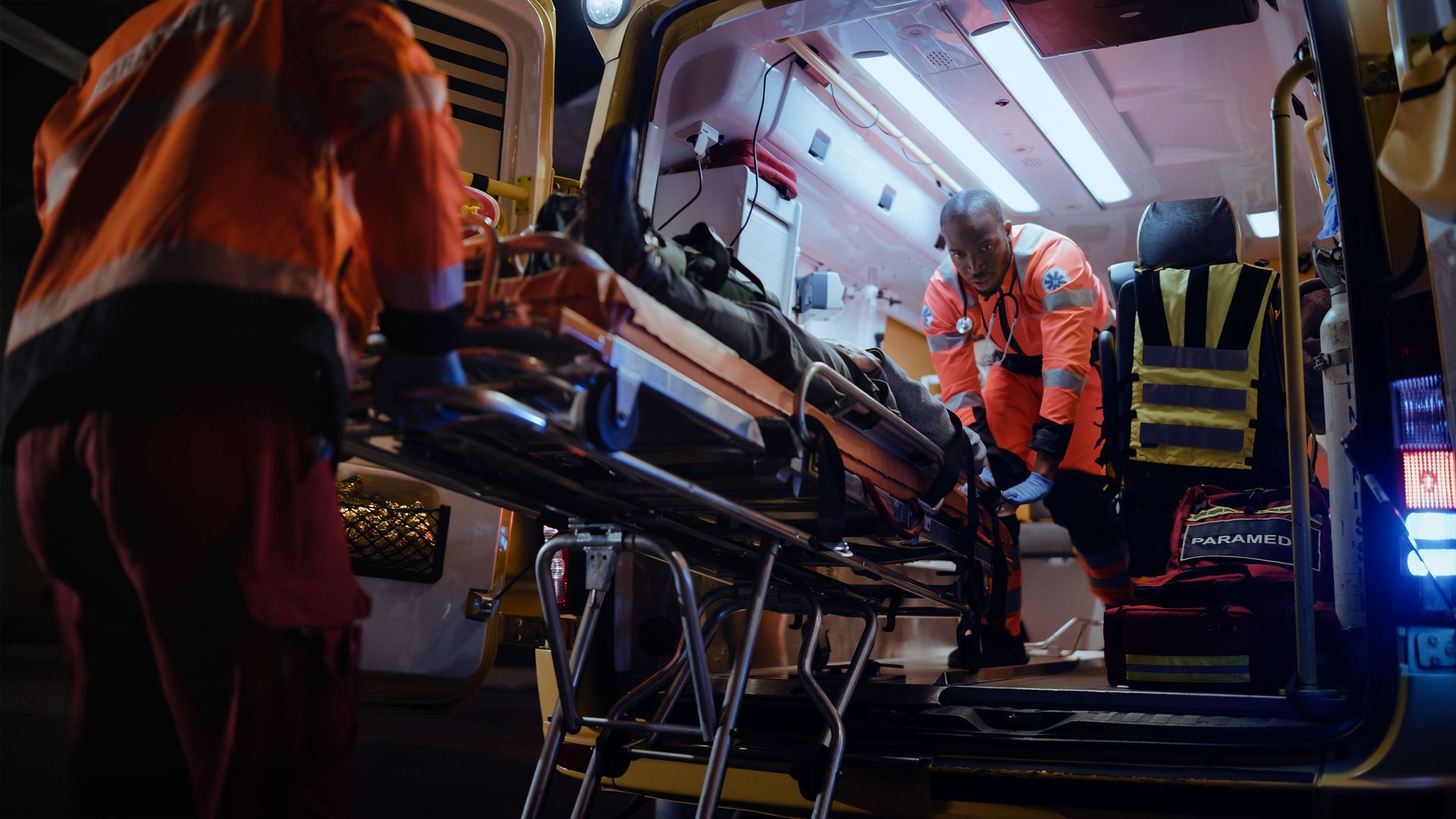 A man is standing in the back of an ambulance with a stretcher.