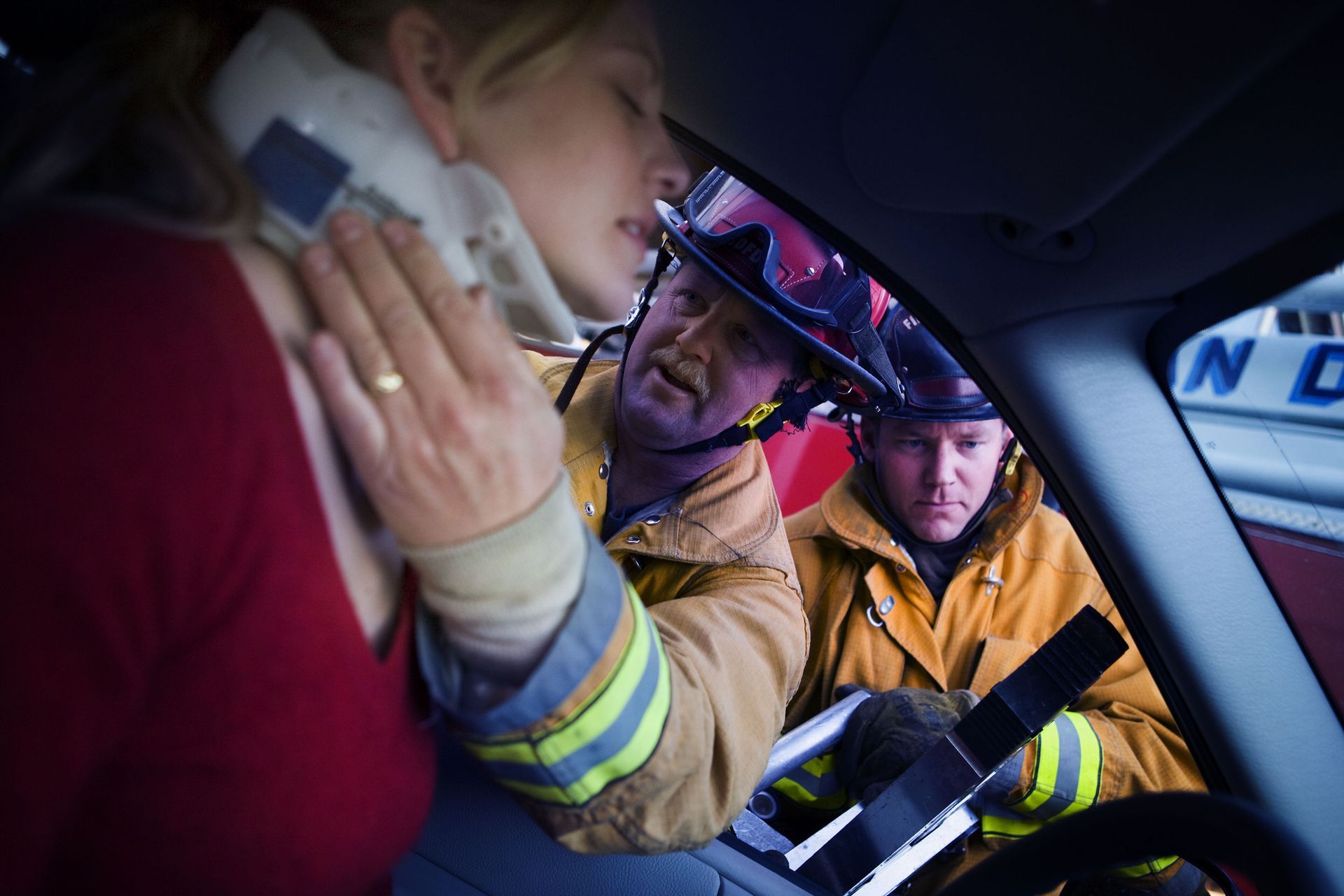 A woman is talking on a cell phone in a car with two firefighters.