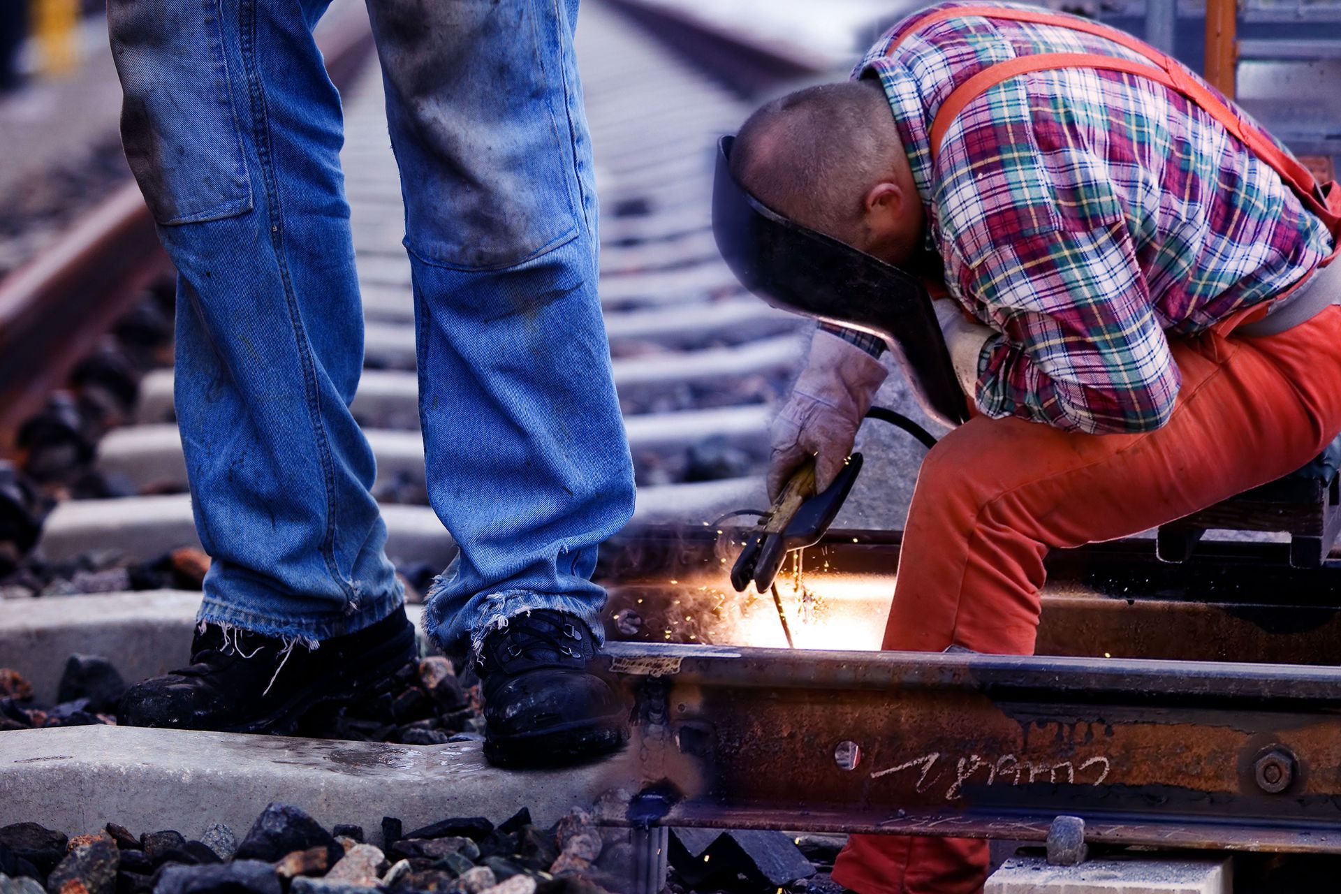 A man wearing a welding mask is working on a train track