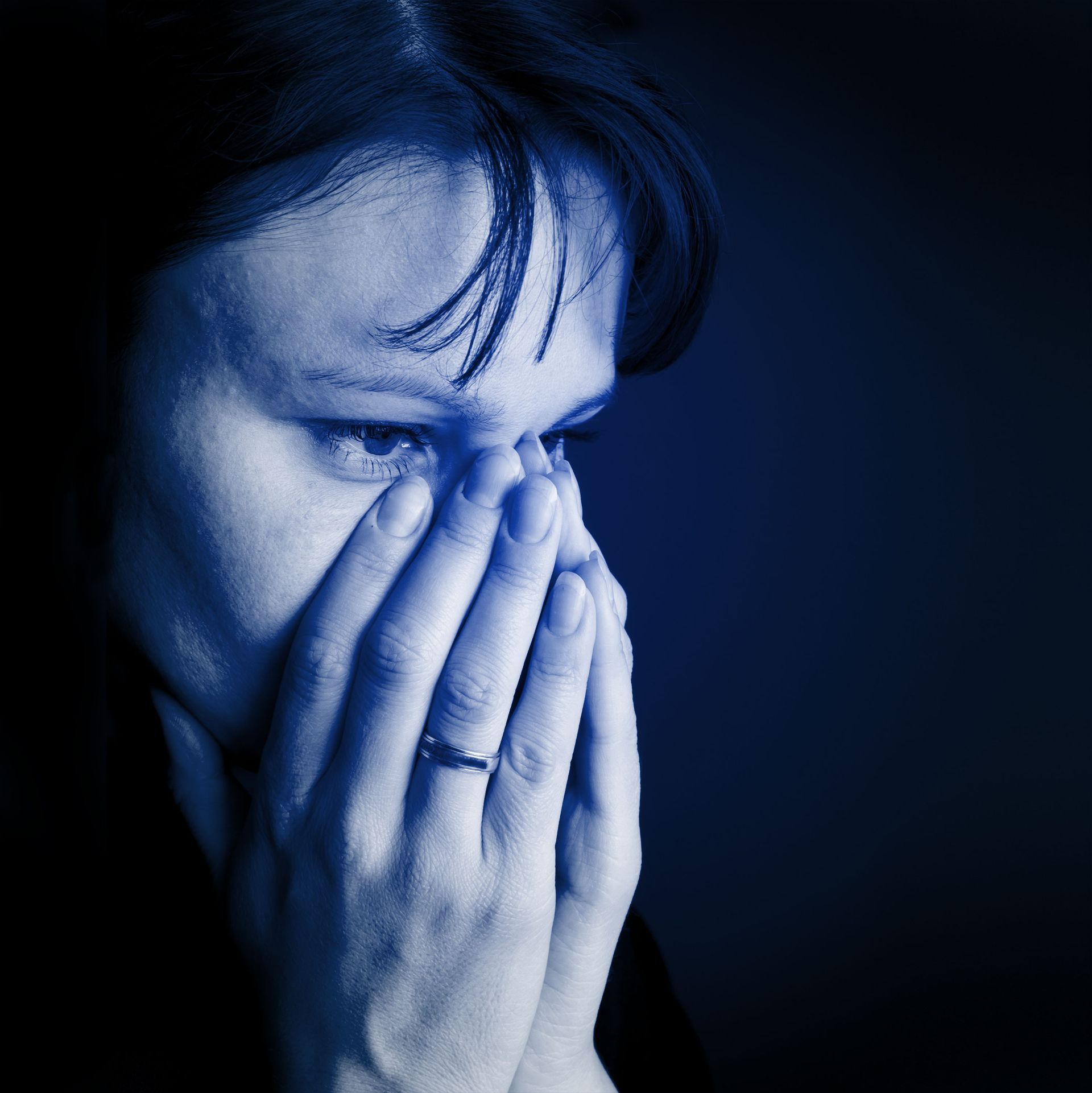 A woman with a ring on her finger is covering her face with her hands