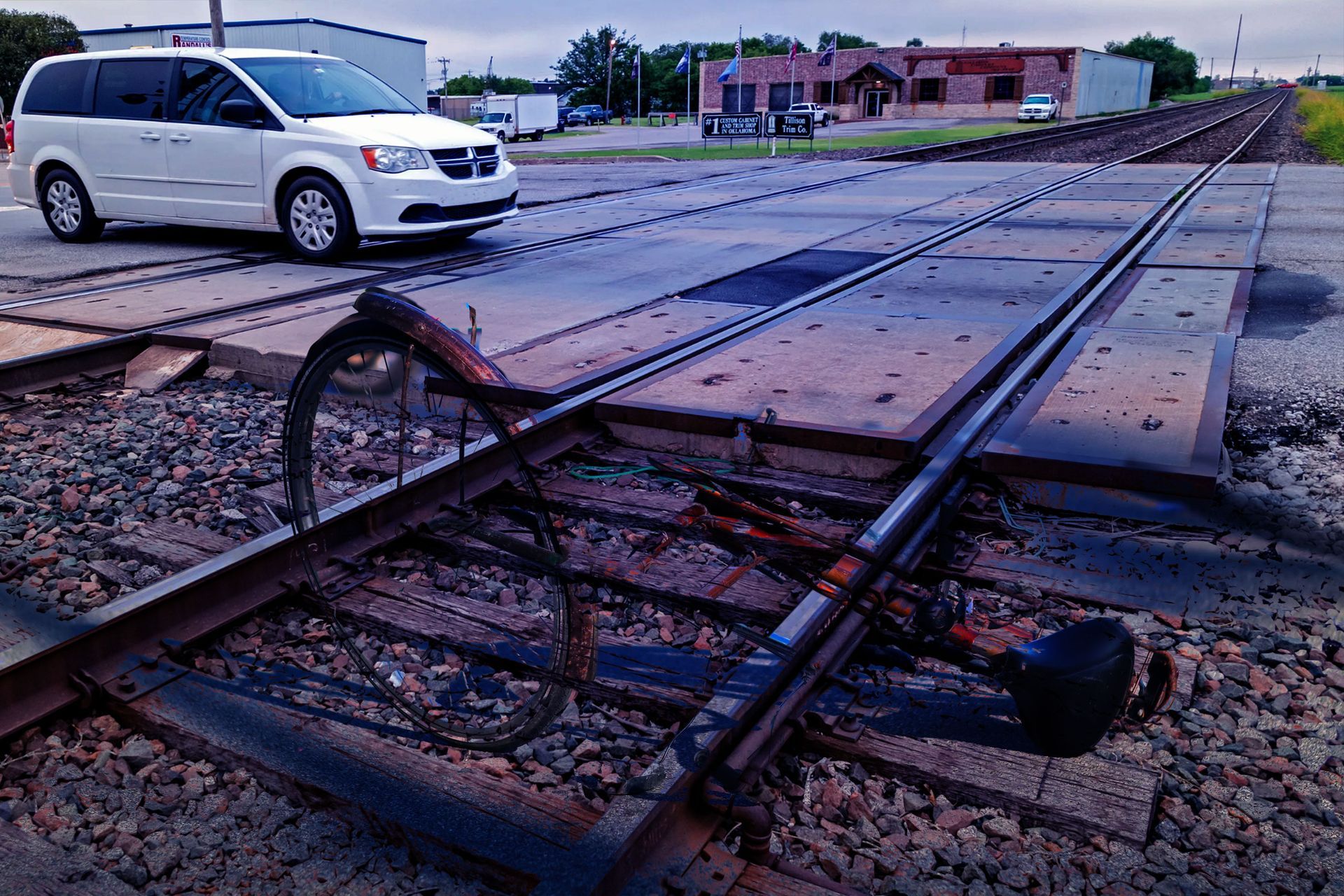 A white minivan is driving down train tracks