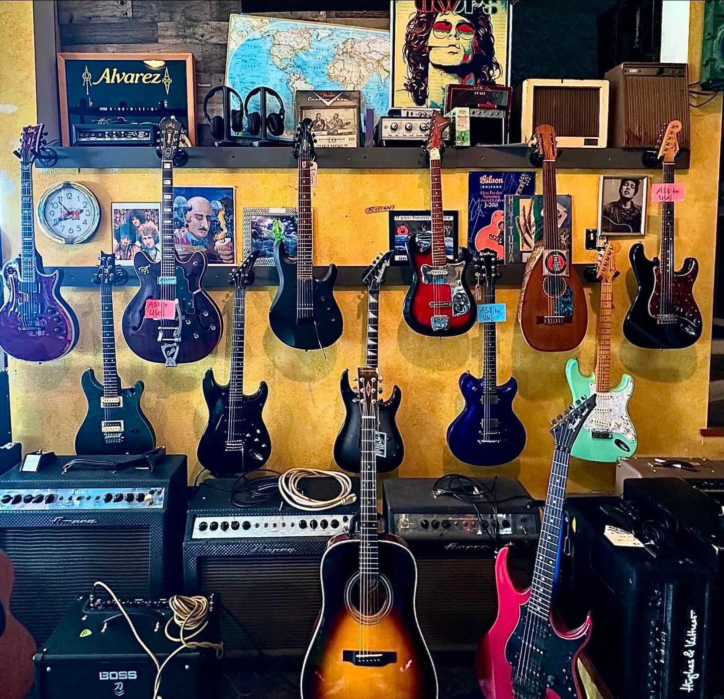 A bunch of guitars are hanging on a wall with a marshall amp in the background