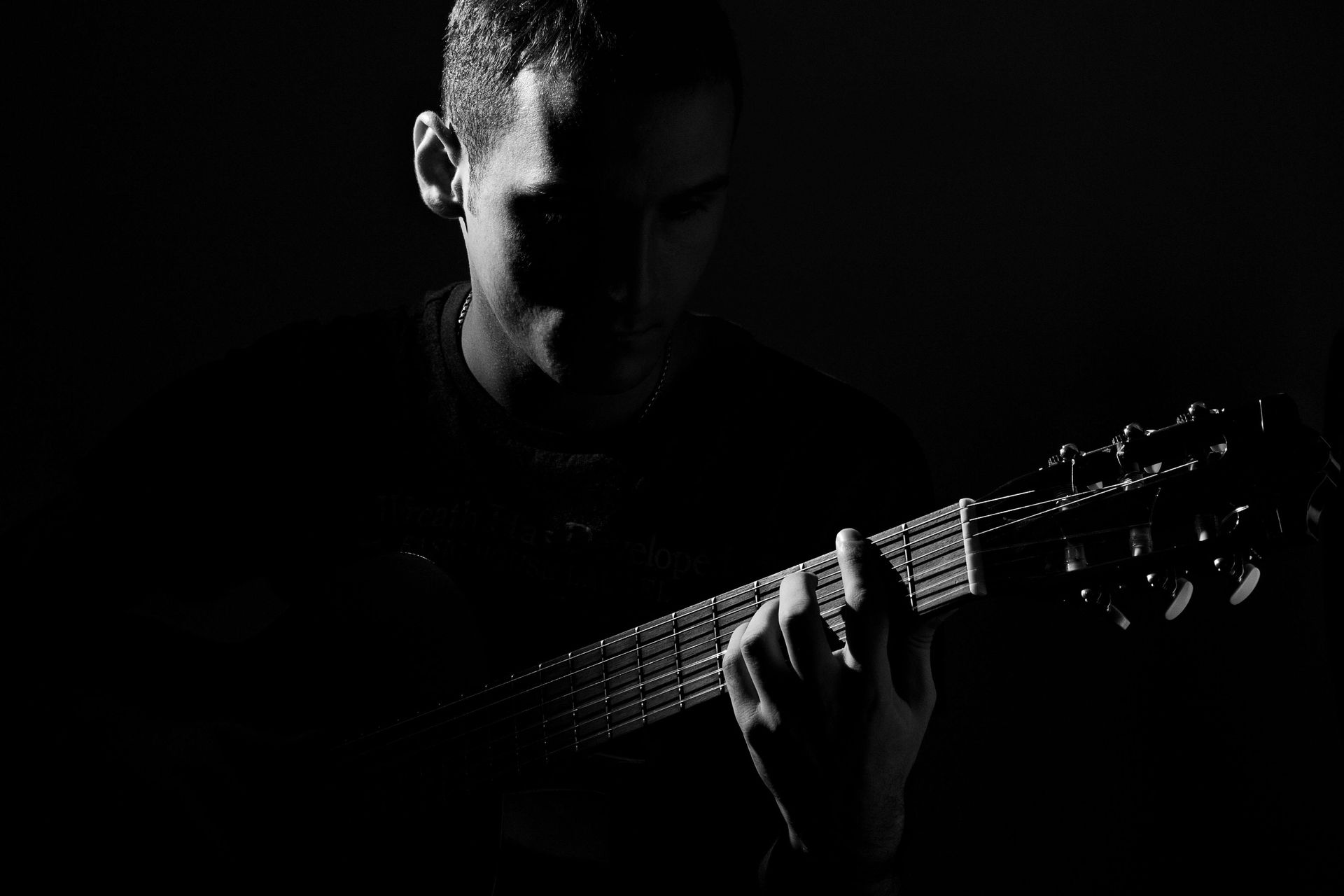 A man is playing a guitar in the dark in a black and white photo.