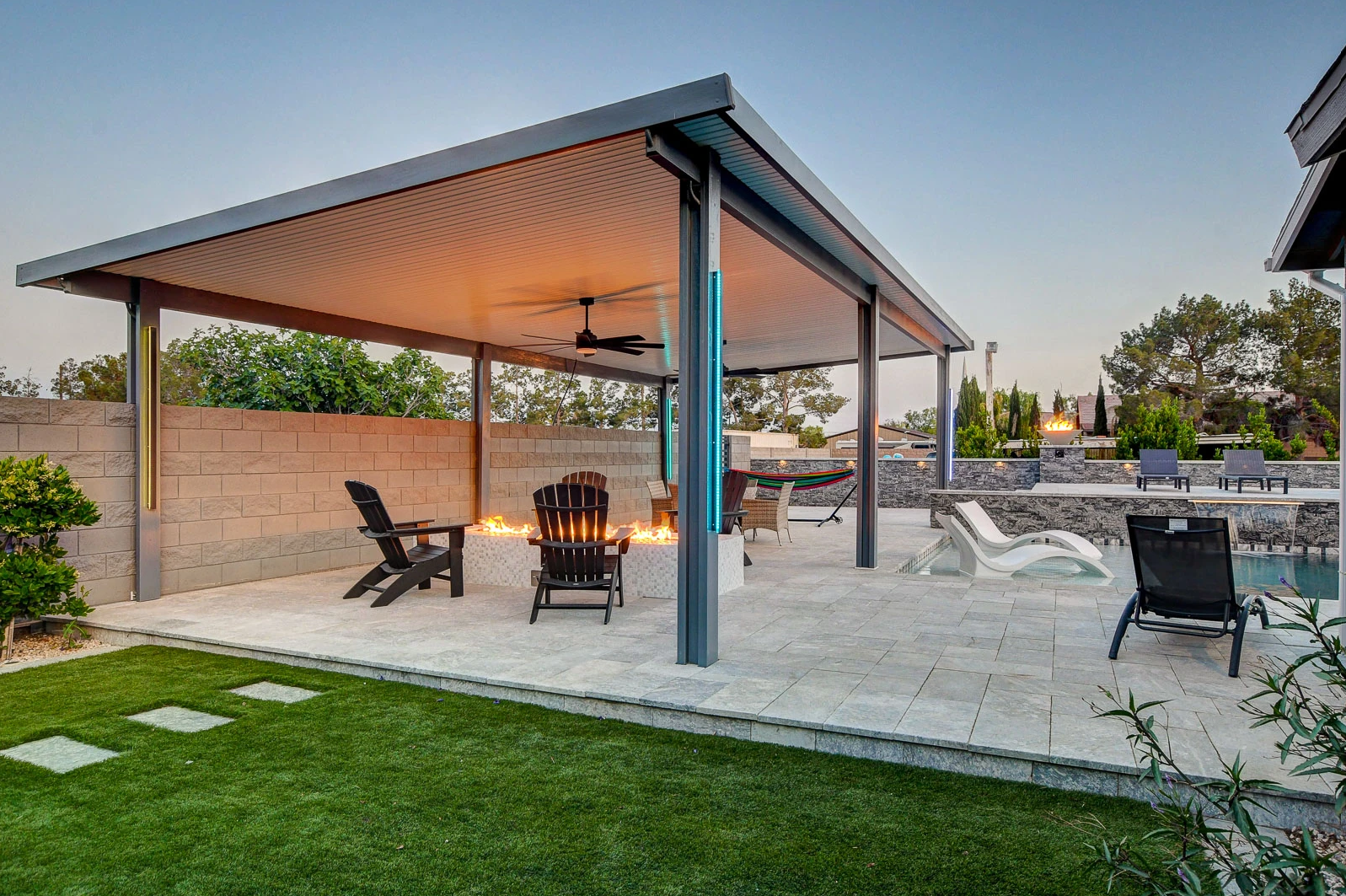 A patio with a pavilion , chairs , a table and a fire pit.