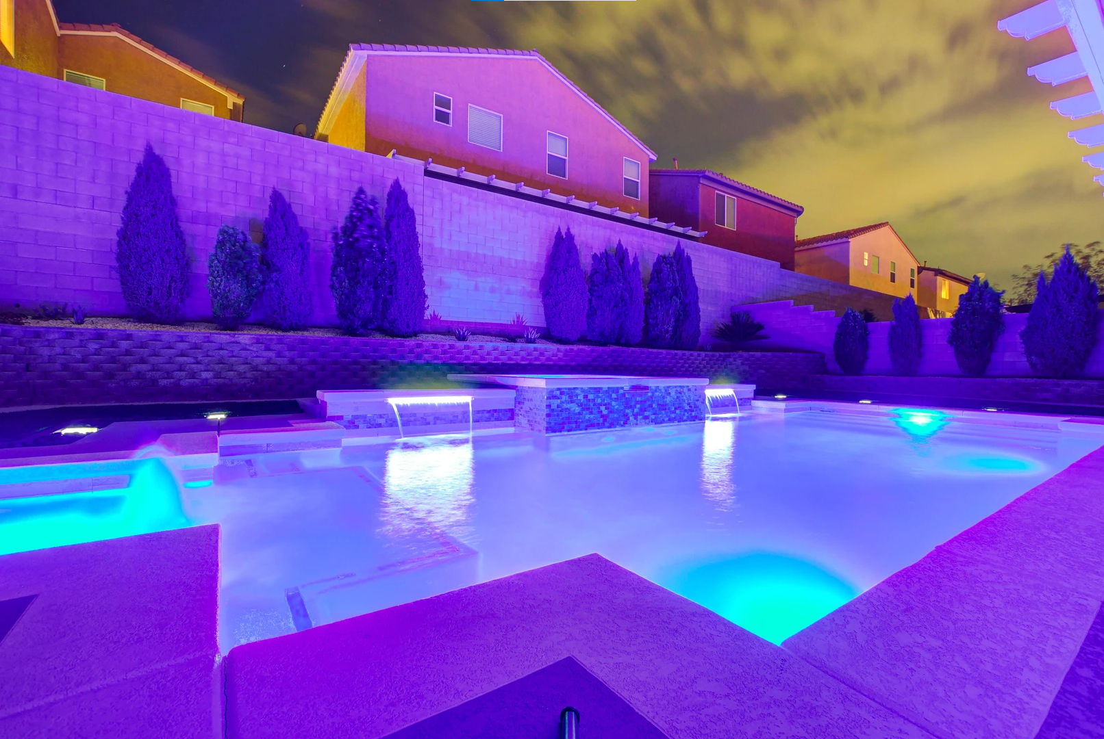 A large swimming pool is lit up with purple lights at night.