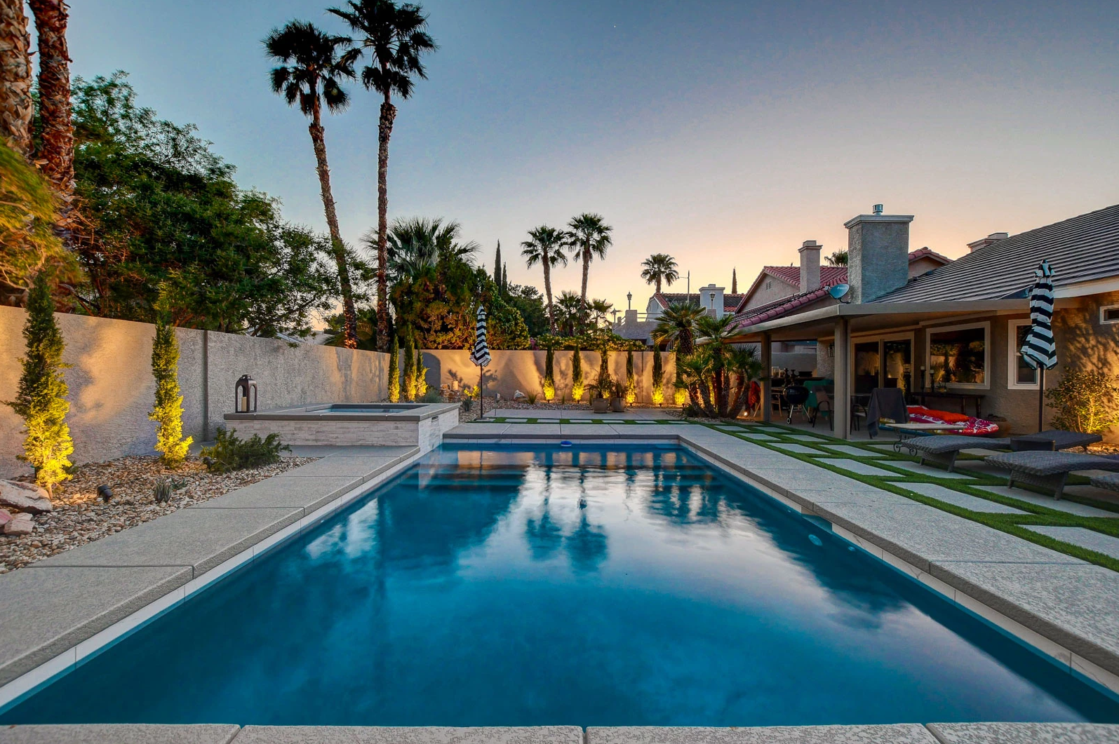 A large swimming pool in the backyard of a house with palm trees in the background.