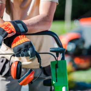 A man wearing gloves and ear muffs is pushing a green lawn mower