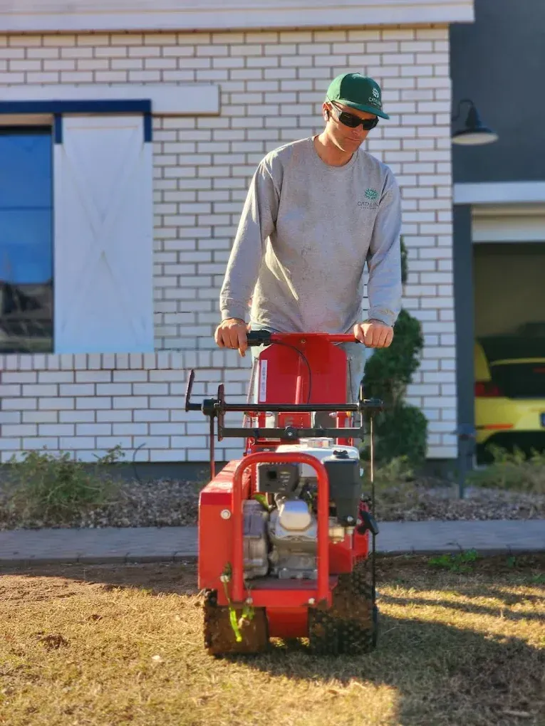 A man is standing next to a red lawn mower in front of a brick house.