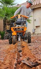 A man is using a trencher to dig a hole in the ground.