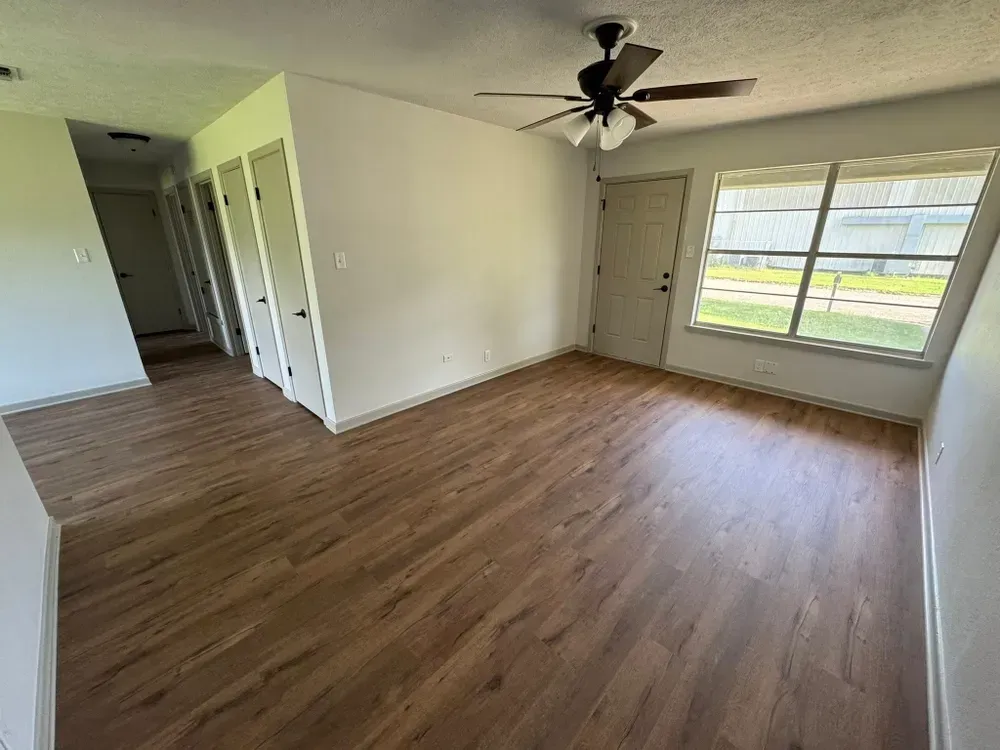 Empty room with wood-look flooring, white walls, closet doors, and a window.
