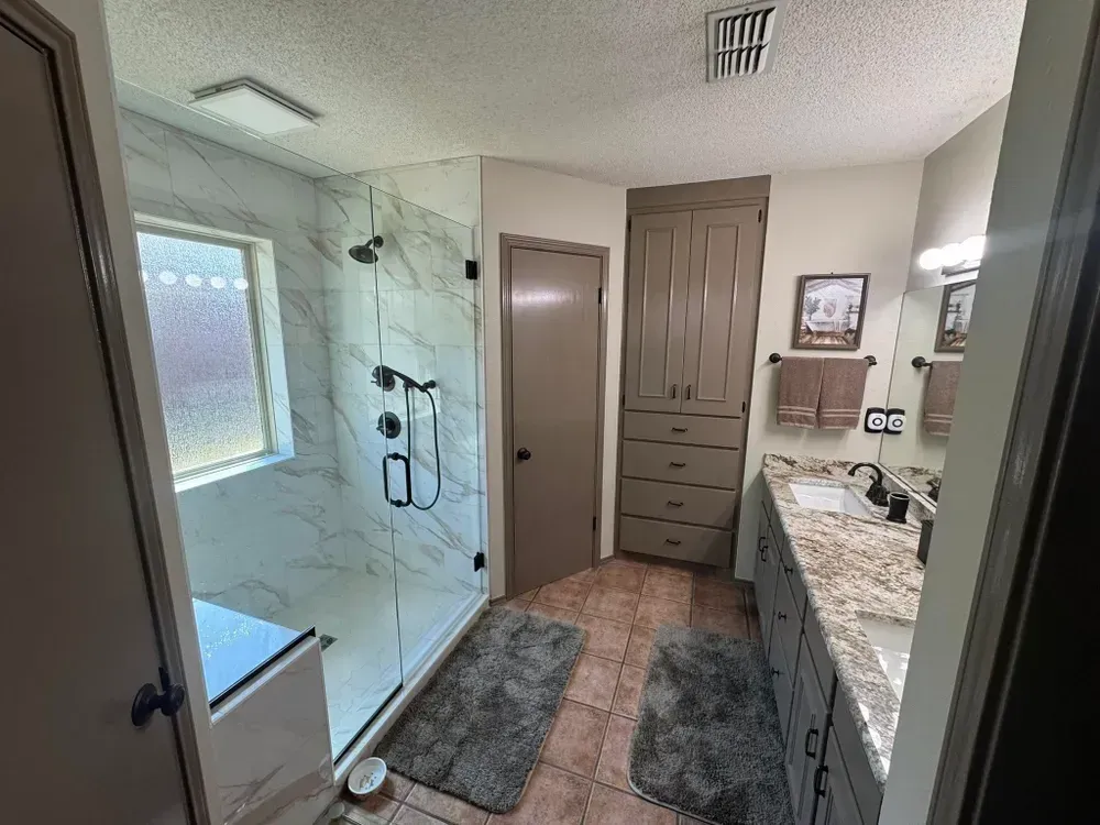 Bathroom with a marble-tiled shower, long vanity, and a tall cabinet. Gray, brown, and white color scheme.