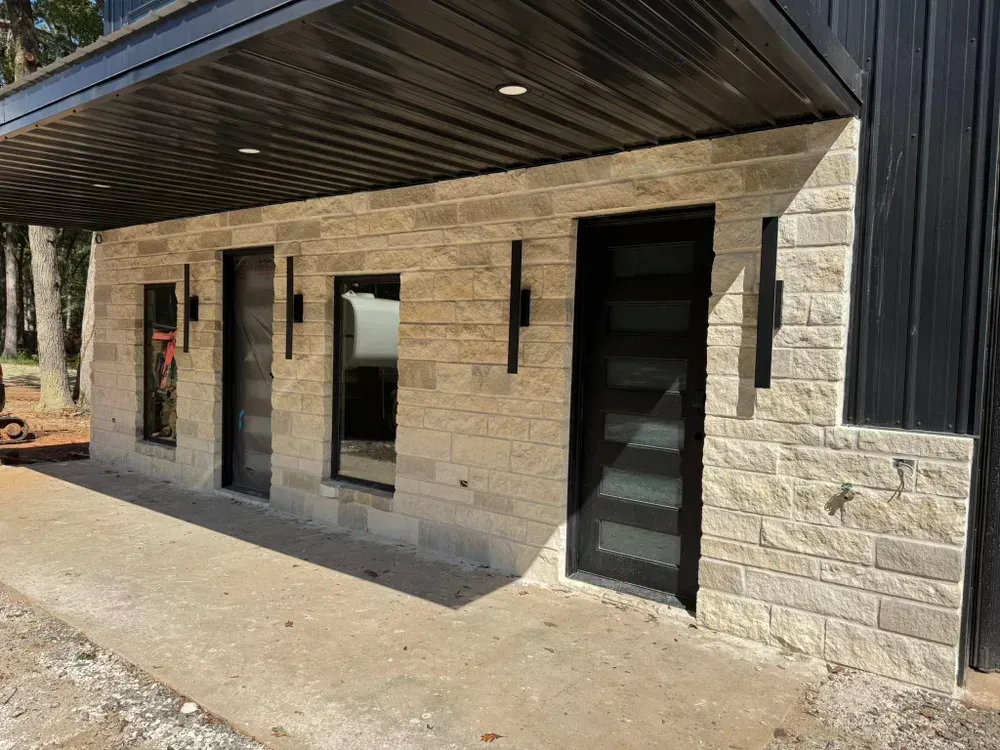 Building exterior with stone facade, black trim, and door, under a black awning.