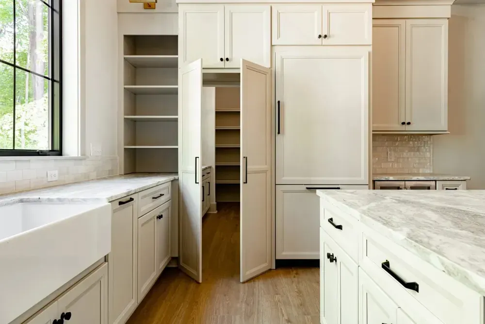 Cream kitchen with open pantry, cabinets, and island with a window and white countertop.