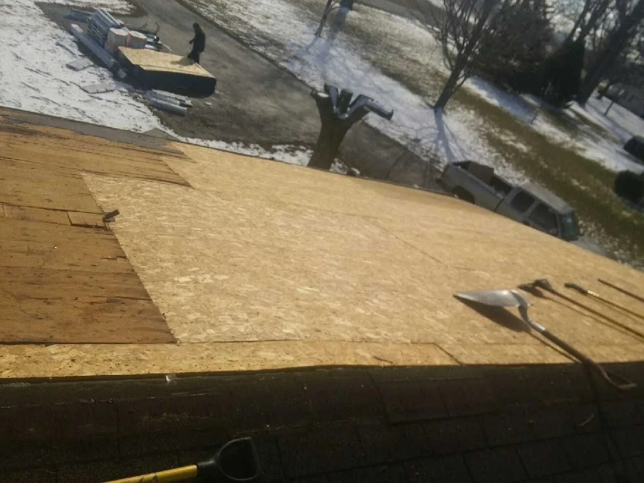 Rooftop with installed OSB sheathing. A person stands on the roof. Tools and snow are visible nearby.