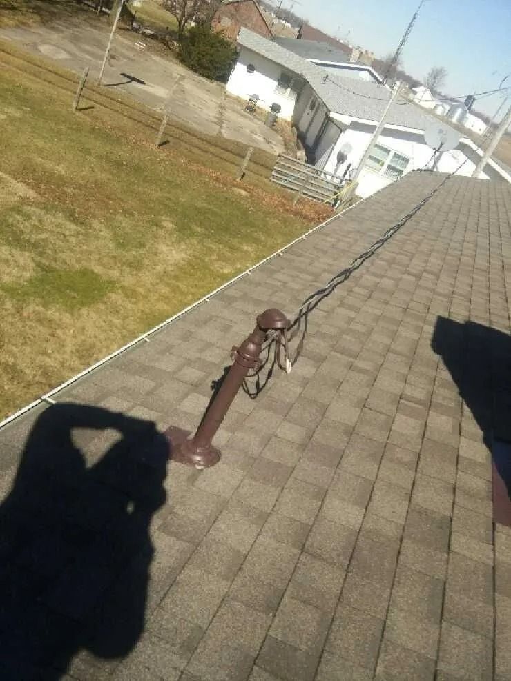 Shadow of person holding camera, roof with brown shingles, vent pipe, overhead wires, and houses in background.