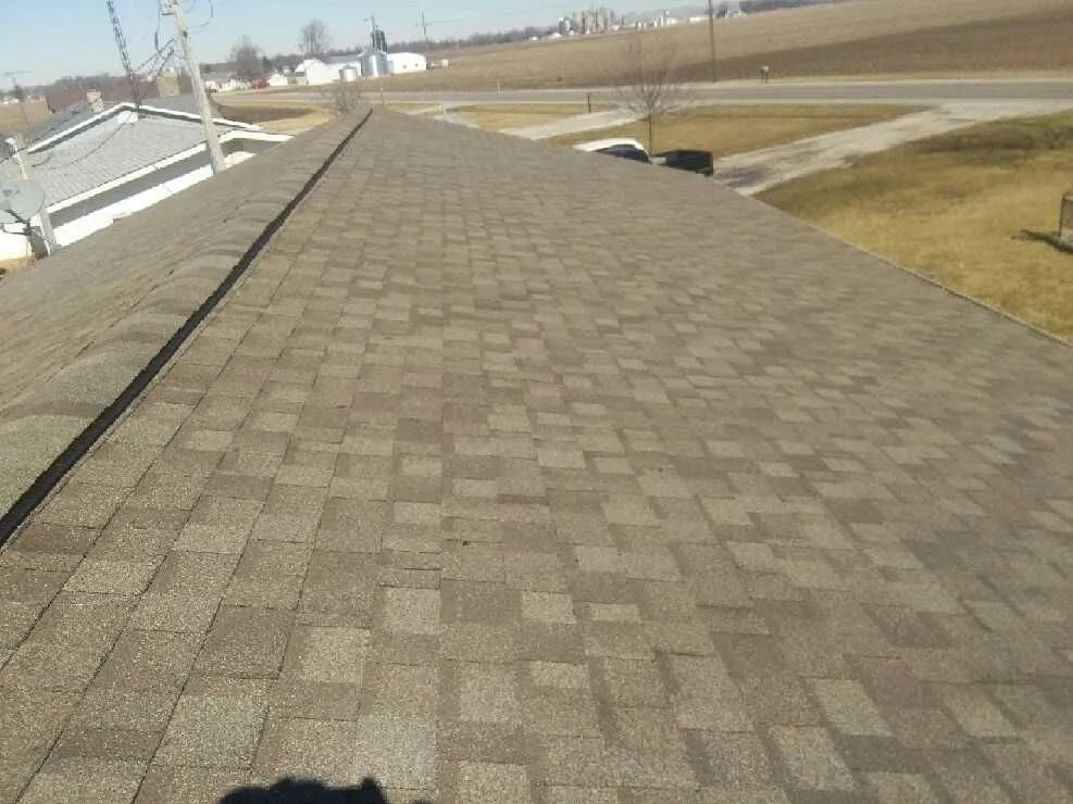 Brown asphalt shingle roof on a house, angled view, sunny outdoor setting.