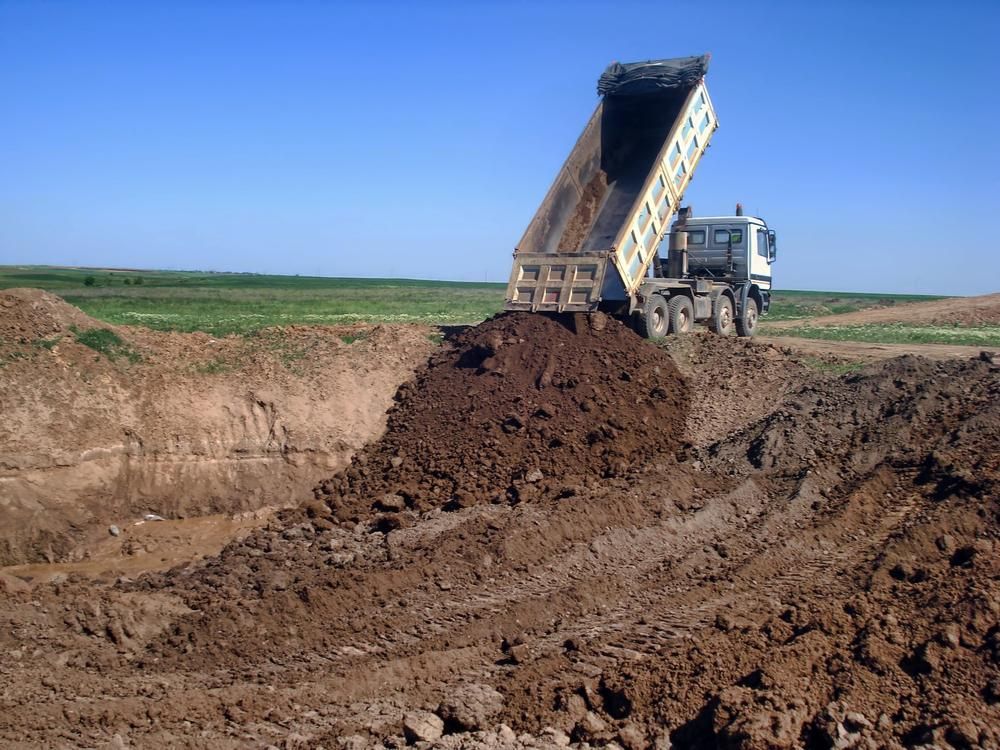 A Dump Truck is Dumping Dirt Into a Hole — Eddy’s Excavations & Bobcat Hire In Gladstone, QLD