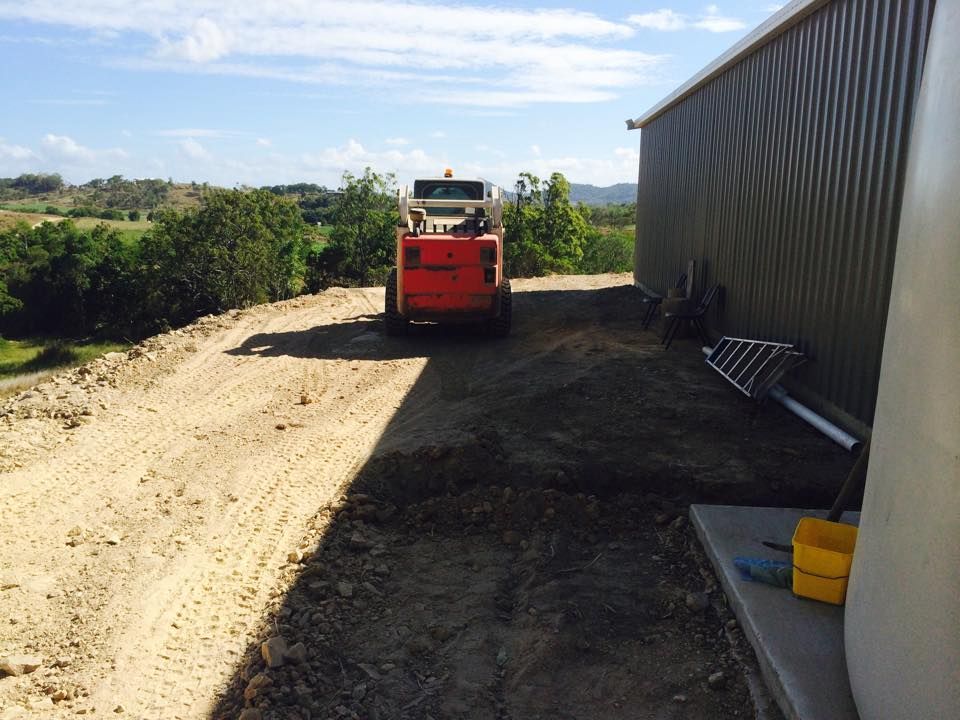 A Truck is Driving Down a Dirt Road Next to a Building — Eddy’s Excavations & Bobcat Hire In Wurdong Heights, QLD