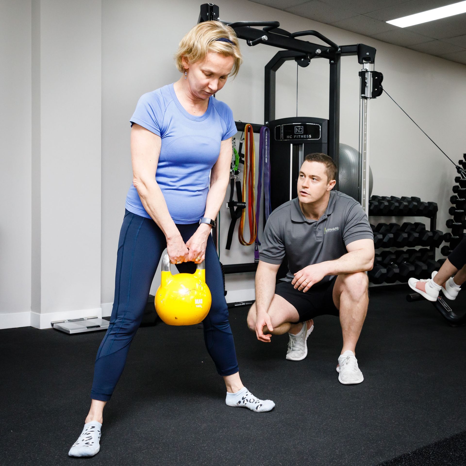 A man squatting next to a woman holding a yellow kettlebell