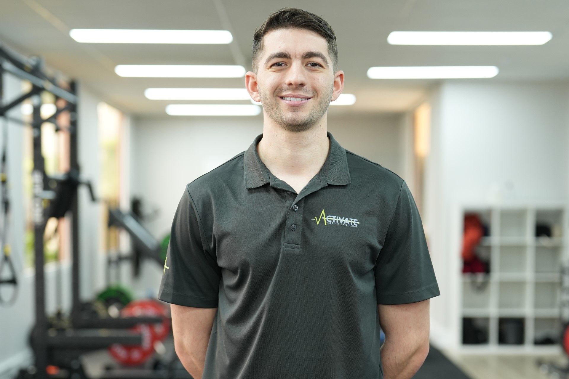 A man in a black polo shirt is standing in a gym.