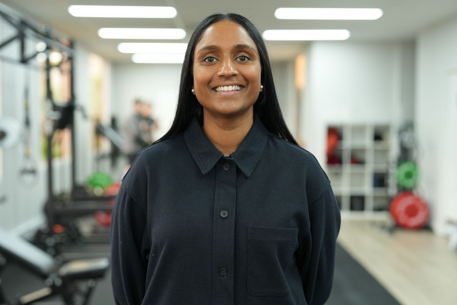 A woman in a black shirt is smiling in a gym.