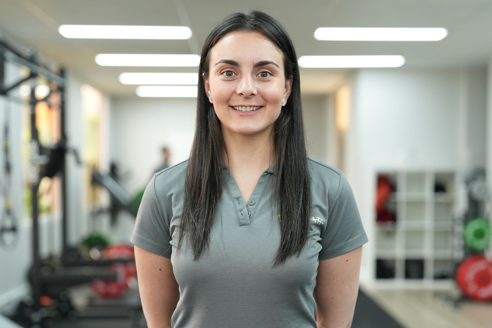 A woman is standing in a gym and smiling for the camera.