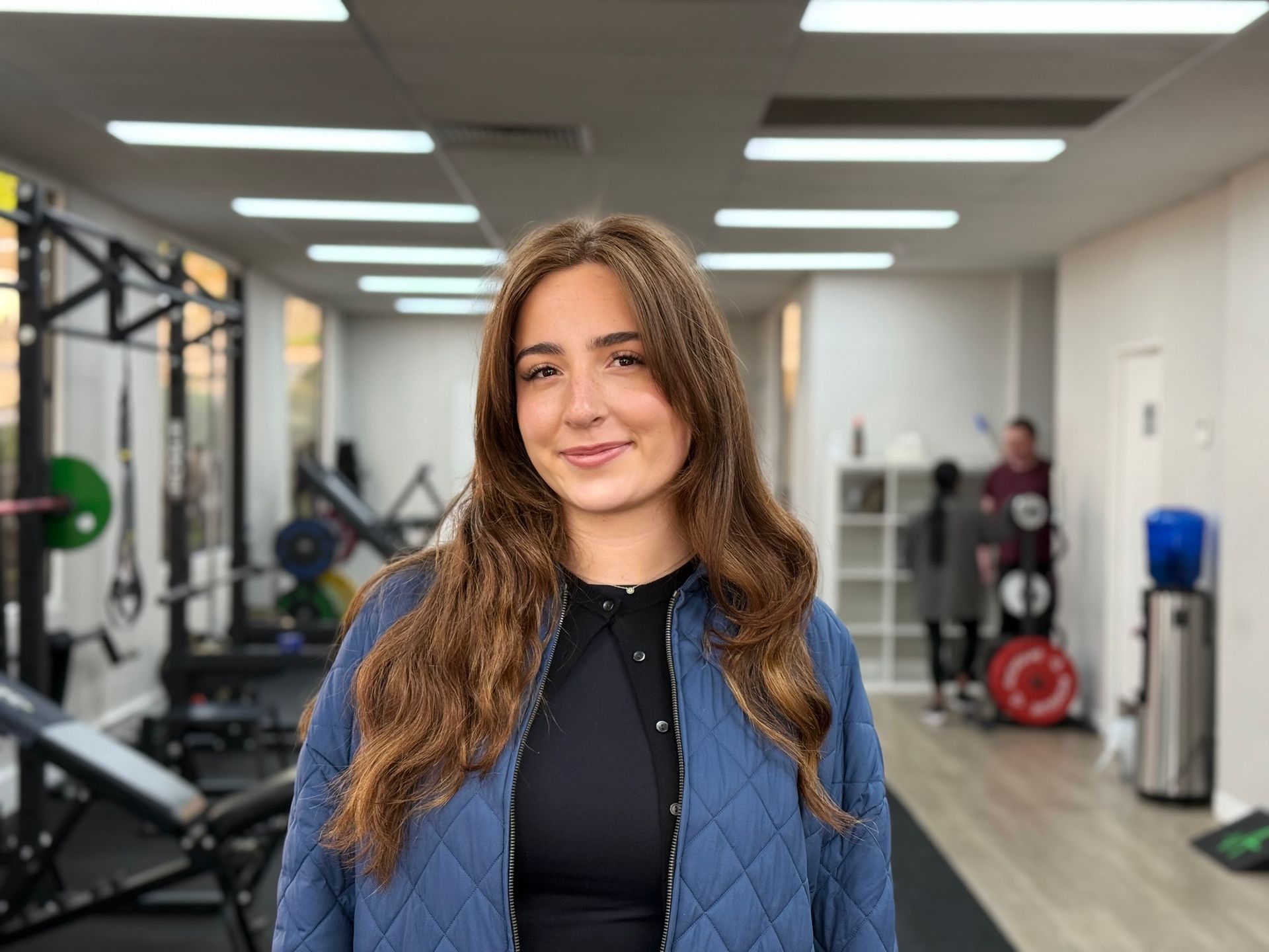 A woman in a blue jacket is standing in a gym.