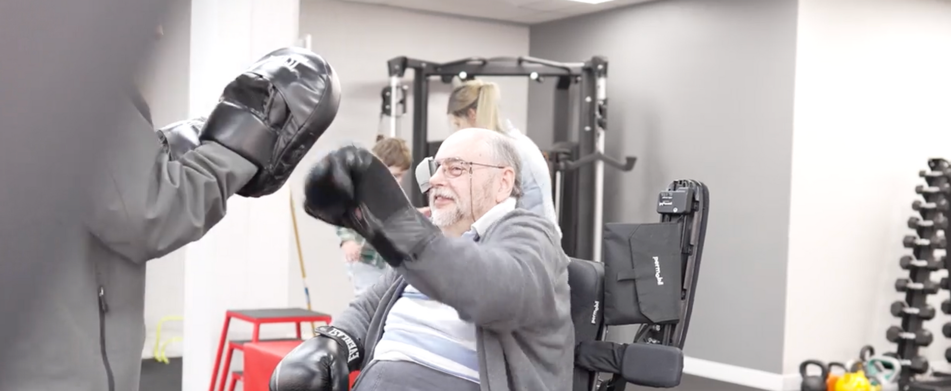 An elderly man is wearing boxing gloves in a gym.