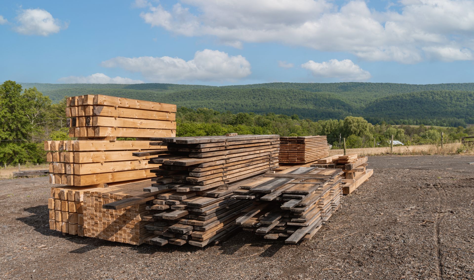 A pile of wood in a gravel area with mountains in the background