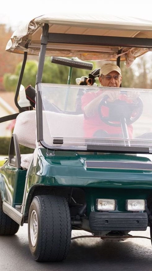A man is driving a green golf cart down a street.