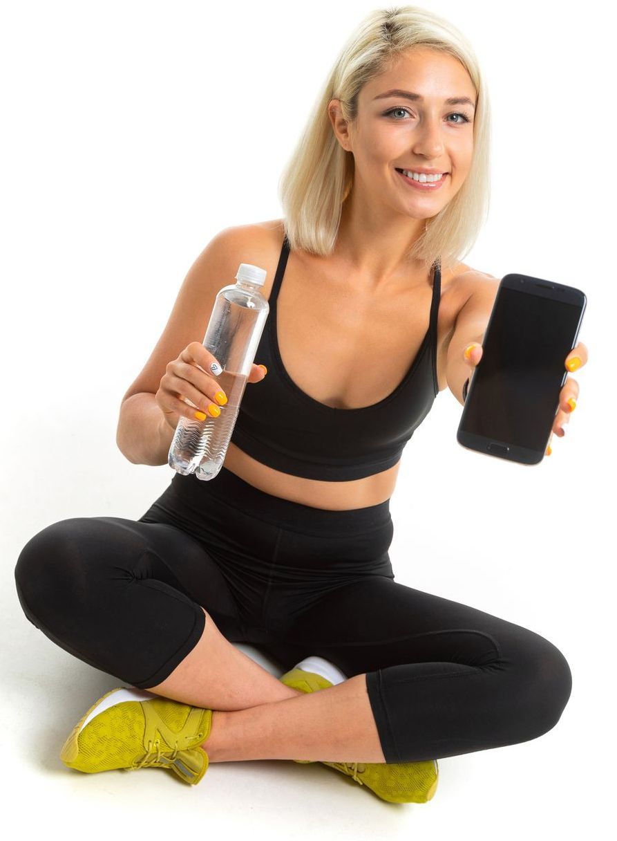 A woman is sitting on the floor holding a bottle of water and a cell phone.