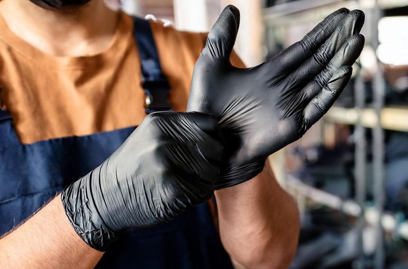 Person putting on black gloves. Indoors, wearing a blue apron over a tan shirt.