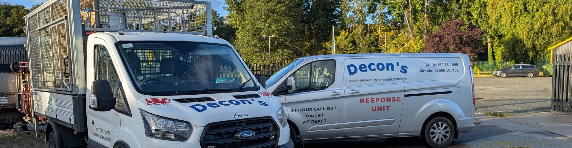 Two white Decon's vans parked side-by-side, near trees and a building in the background.