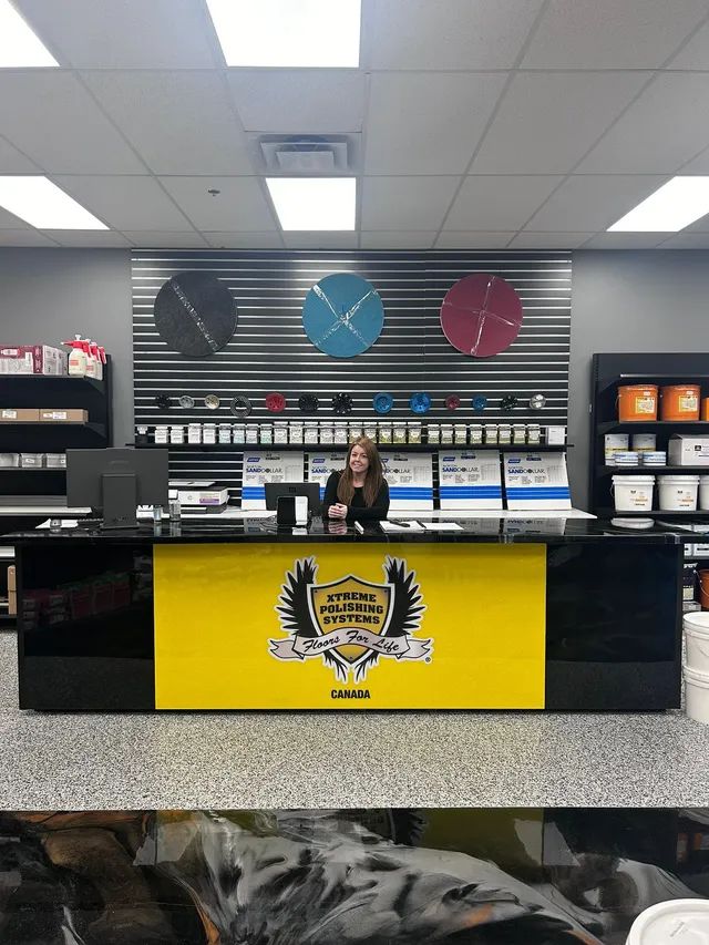 Woman at a business counter with logo. Behind her are colored clocks and product samples.