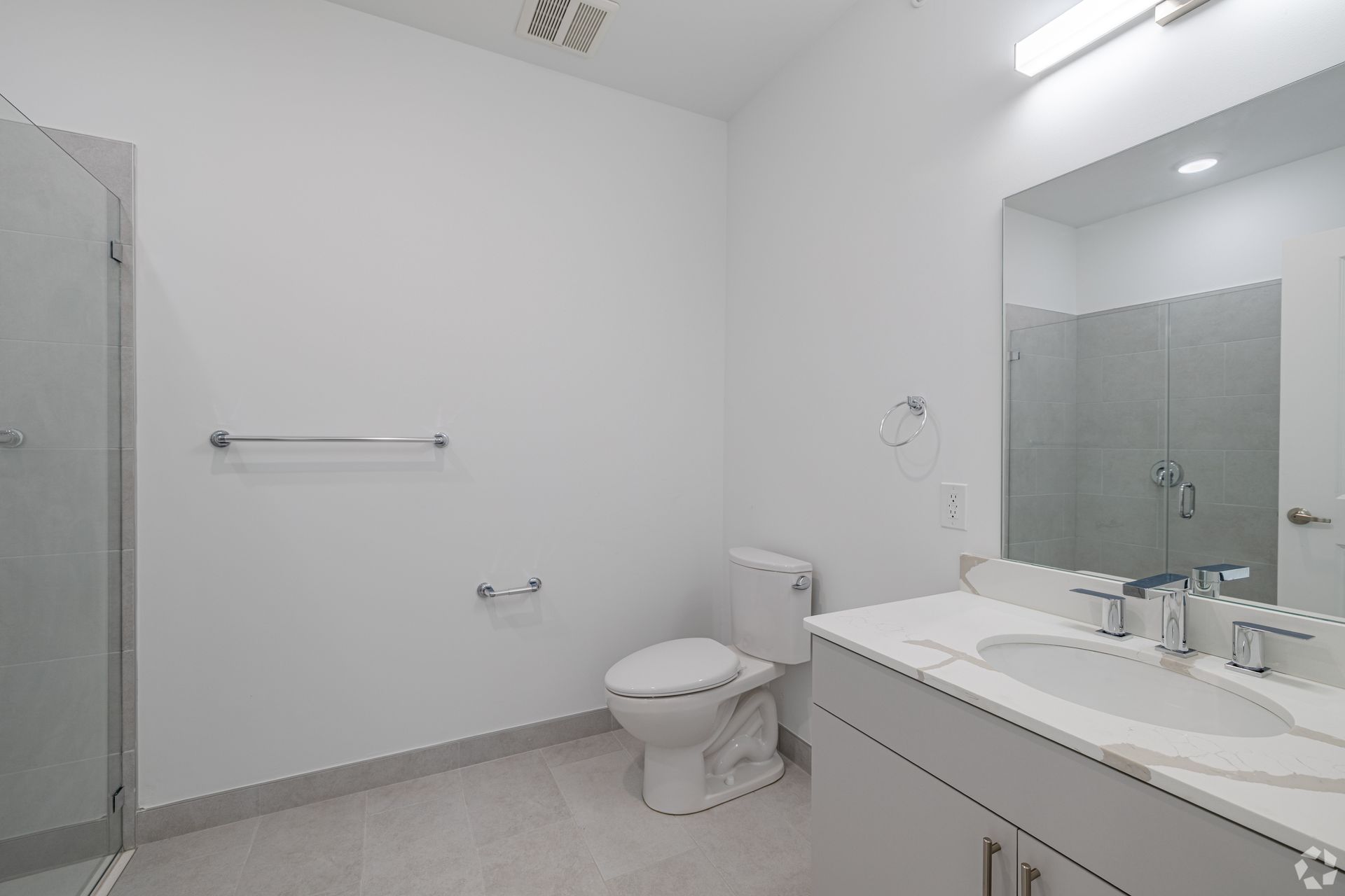 Basketball court with surrounding buildings, trees, and fencing on a sunny day.