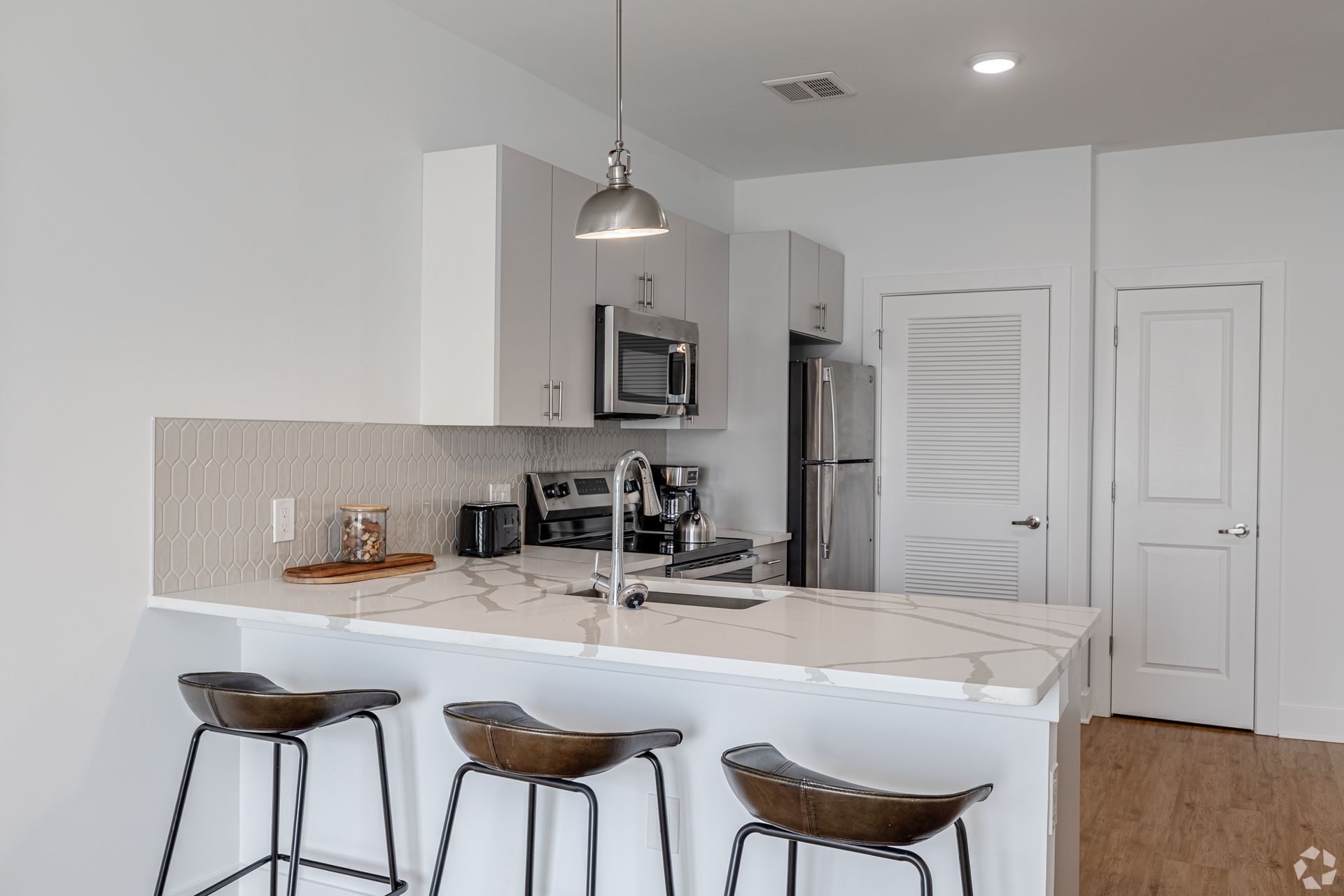 Bedroom with bed, artwork, and a doorway leading to a bathroom. Light gray walls and wood flooring.