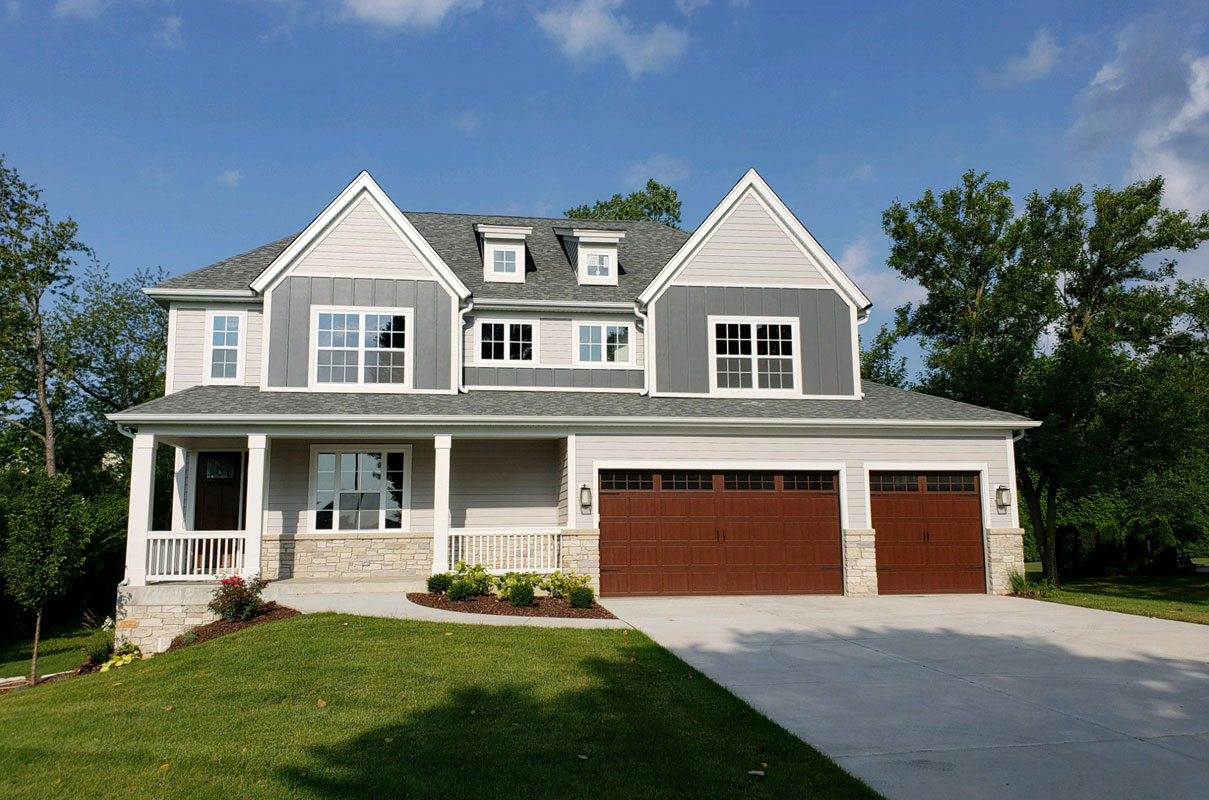 Two-story house with gray siding, brown garage doors, and a green lawn.