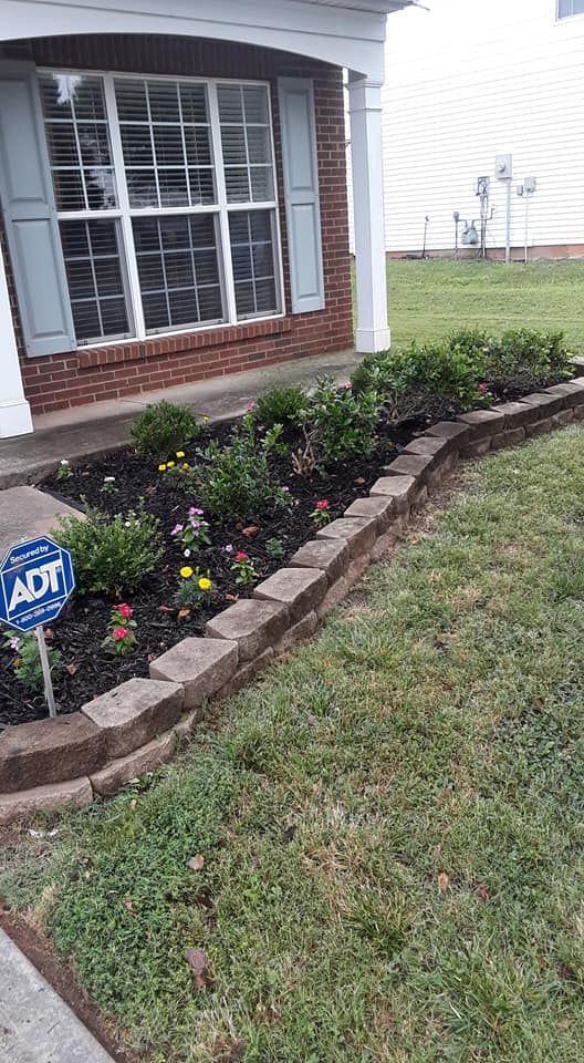 A brick house exterior with a flower bed edged by stone blocks and an ADT security sign in the mulch.