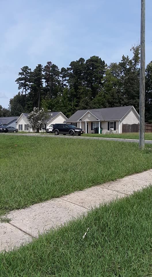 A street view showing two one-story suburban houses behind a grassy lawn, with a dark SUV parked in a driveway.