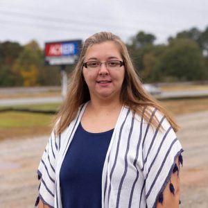 A woman wearing glasses and a striped shirt is standing in front of a sign.